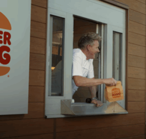 A chef hanging out of a video at a drive thru.